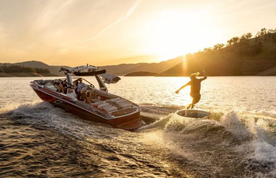 A kid wake surfing behind a red Centurion boat at sunset.